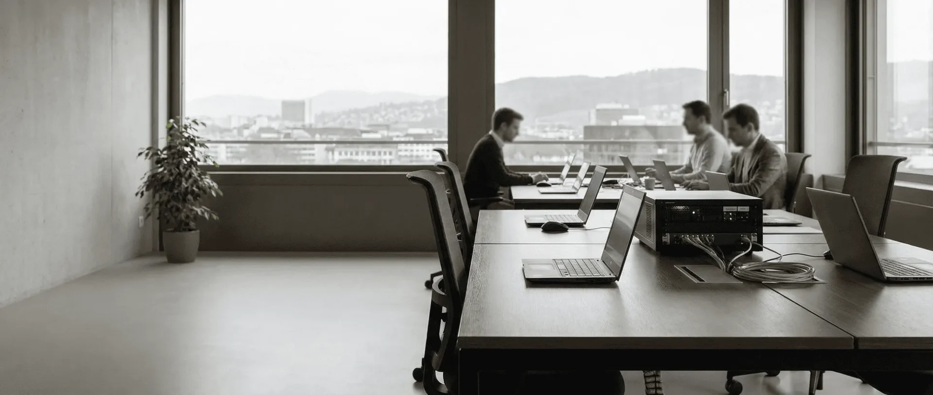 Besprechungsraum mit Mitarbeitern an Laptops bei der Arbeit, modern eingerichtet mit großer Fensterfront und Blick auf die Stadt.