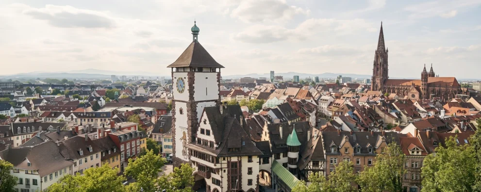 Blick über die Altstadt von Freiburg mit einem historischen Stadttor vorne und dem Freiburger Münster rechts